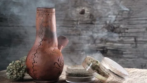 Steaming bong with cannabis on the table on which there is a grinder and a large Stock Footage 134940638