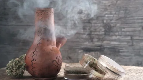 Steaming bong with cannabis on the table on which there is a grinder and a large Stock Footage 134940746