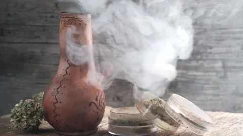 Steaming bong with cannabis on the table on which there is a grinder and a large Stock Footage 134940801