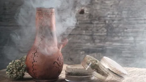 Steaming bong with cannabis on the table on which there is a grinder and a large Stock Footage 134940891