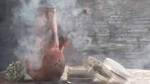 Steaming bong with cannabis on the table on which there is a grinder and a large Stock Footage 134940963
