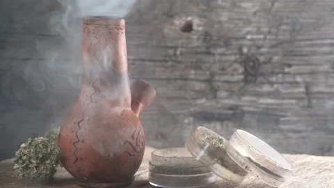 Steaming bong with cannabis on the table on which there is a grinder and a large Stock Footage 134941069