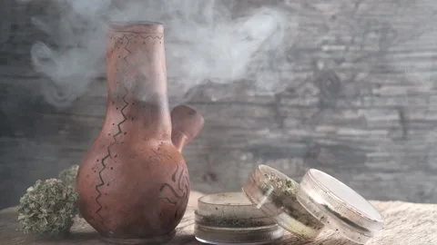 Steaming bong with cannabis on the table on which there is a grinder and a large Stock Footage 134941330