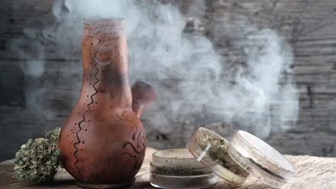 Steaming bong with cannabis on the table on which there is a grinder and a large Stock Footage 134941649