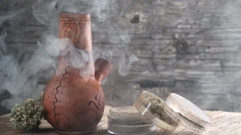 Steaming bong with cannabis on the table on which there is a grinder and a large Stock Footage 134942195