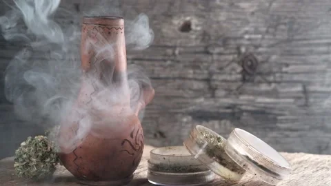 Steaming bong with cannabis on the table on which there is a grinder and a large Stock Footage 134942299