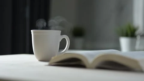 Steaming Coffee Mug on Cozy Table with Open Book Calm Still Life in a Cozy Room Stock Footage 295802089