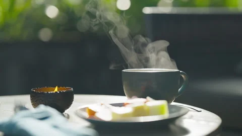 Steaming cup of tea with fruit slices and lit candle on outdoor table setting Video stock 328043279