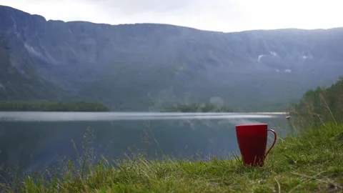 A steaming cup of tea or coffee in front of a mountain lake Stock Footage 165183607