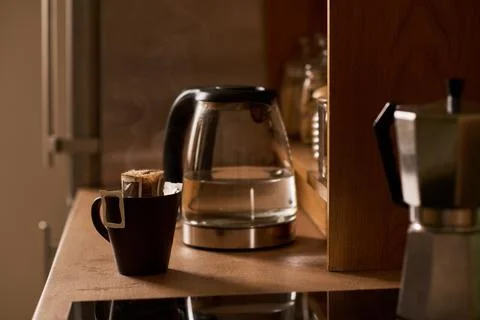 Steaming Drip Bag Coffee Mug Beside Electric Kettle at Home Fotos de archivo