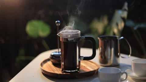 Steaming French press coffee maker with cups on a table outdoors at dusk Stock Footage 338990682