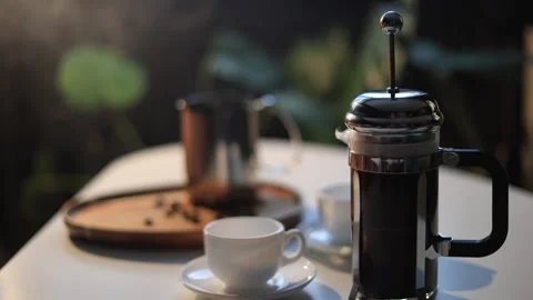 Steaming French press coffee maker with cups and beans on a table outdoors Stock Footage 338990751