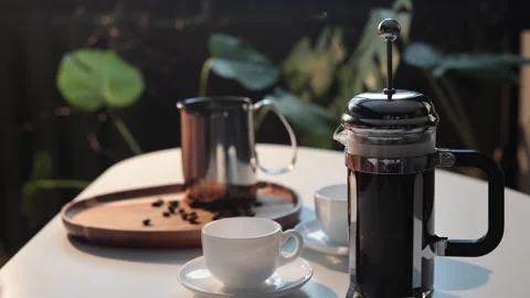 Steaming French press coffee maker with cups and beans on a table Stock Footage 338990754