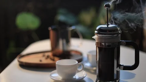 Steaming French press coffee maker with espresso cups and coffee beans on a Stock Footage 338990786