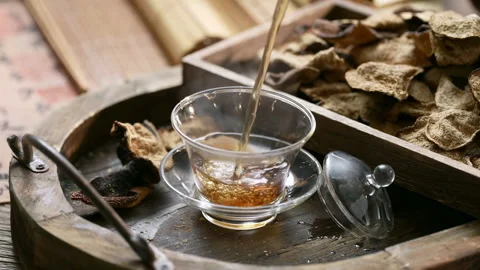 Steaming herbal Tea on a wooden table with herbs and tangerine is poured into a Stock Footage 308005763
