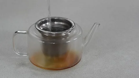 Steaming hot black tea being slowly poured from a teapot into a clear glass cup. Stock Footage 303495305