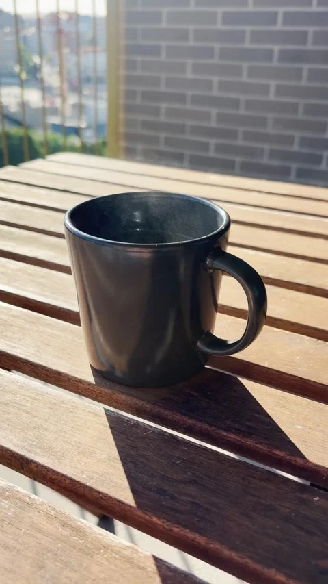 Steaming hot coffee mug resting on a wooden table in the morning sunlight Stock Footage 345694178