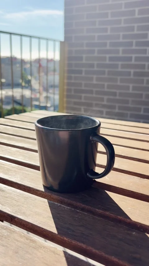 Steaming hot coffee mug resting on a sunny balcony table Stock Footage 345889183