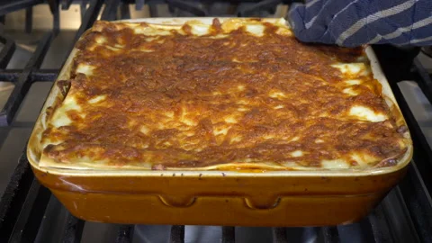 Steaming hot lasagne in a baking dish on an oven hob (1 of 3). Stock Footage 143454680