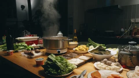 Steaming Hot Pot and Abundant Ingredients on a Wooden Table Indoors at Night in Stock Footage 342159239