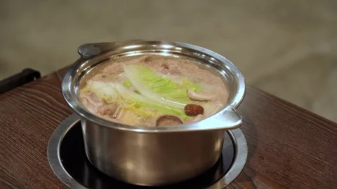 A steaming hot pot on a wooden table, offering a warm dining experience. Stock Footage 337949421
