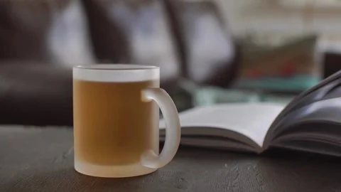 Steaming mug of tea next to an open book Stock Footage 333836842