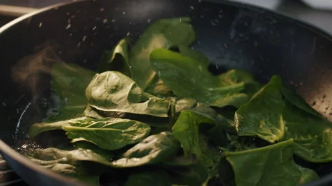 Steaming spinach in a hot frying pan sprinkle with salt in slow motion Stock-Footage 150714580