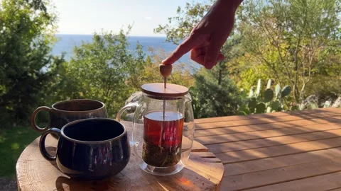 Steaming tea poured into rustic mugs on a wooden table during an outdoor breakfa Video stock 304879520