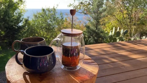 Steaming tea poured into rustic mugs on a wooden table during an outdoor breakfa Video stock 304879547