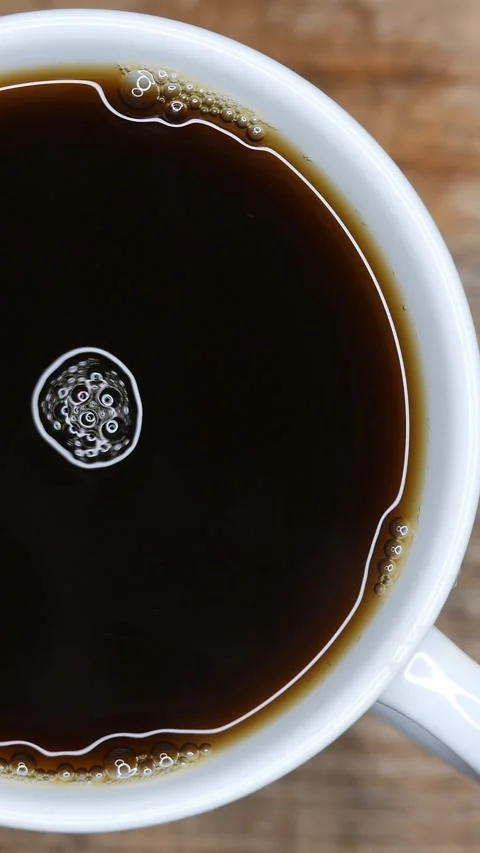 A steamy black coffee cup on the table. Coffee bubbles swirling and popping Stock Footage 272717875