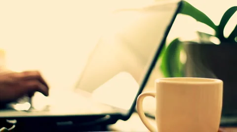 Steamy cup of coffee or tea with man working on laptop in background Stock Footage