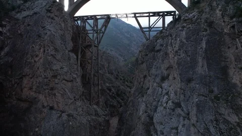 Steel bridge structure towers in deep rocky canyon with mountain walls under Stock Footage 342703974