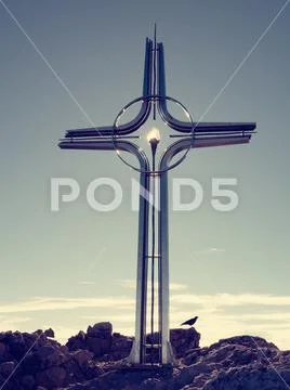 Steel cross raised at mountain summit in Alps. Sharp peak. Daybreak Sun in Stock Photos