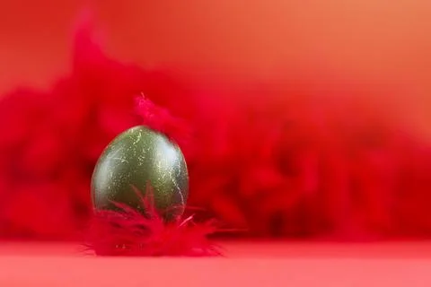 A steel green Easter egg with a feather on the crown against Stock Photos