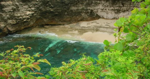 Steep cliff overlooking secluded sandy beach turquoise ocean water crashing wave Stock Footage 344195677