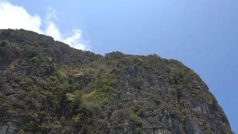 Steep cliffs of the island. Blue sky and a white cloud. The island is covered 스톡 동영상 106966512