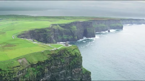 Steep green coastal cliffs with a stone tower on top, aerial shot Видео 348625549