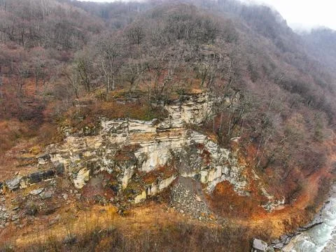 Steep hillside with rock formations, bare trees, and a river below 스톡 사진