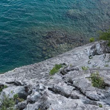 Steep limestone cliff slopes down into the clear turquoise water of a bay Fotos Stock