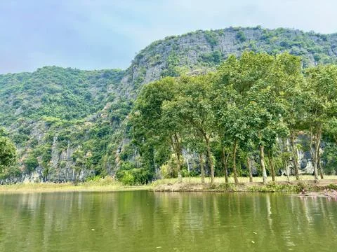 Steep limestone cliffs towering over the green tree line by the banks Stock Photos