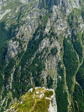 Steep mountain cliffs with rocky formations and green forest cover below Stock Photos