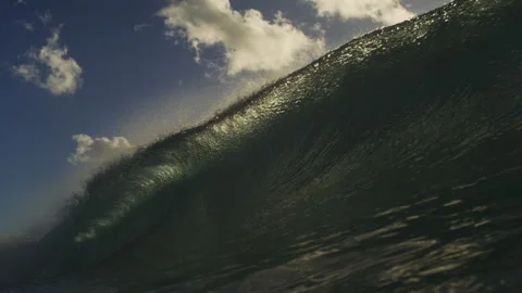 Steep Ocean Wave Rising Beneath Sunlit Clouds and Blue Sky Stock Footage 344377775