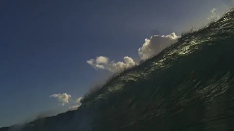Steep Ocean Wave Rising Beneath Sunlit Clouds and Blue Sky Stock Footage 344380773