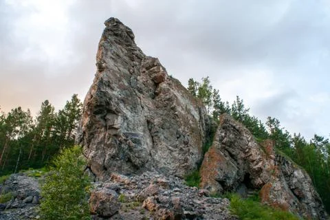Steep rock on a background of cloudy sky and trees. Close-up Stock Photos