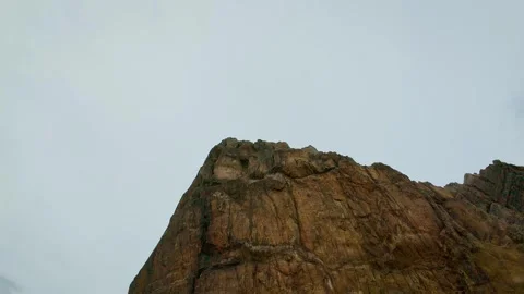 Steep rock formation beneath pale cloudy sky. Monumental cliff face with layered Stock Footage 340326062