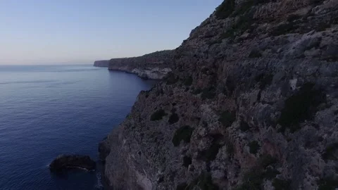 Steep Rocky Cliff Face along a Blue Coastline at Dusk, Aerial Shot Vídeo Stock 340629566