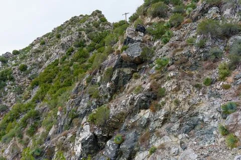 Steep Rocky Cliff Face with Sparse Vegetation and Power Pole 스톡 사진