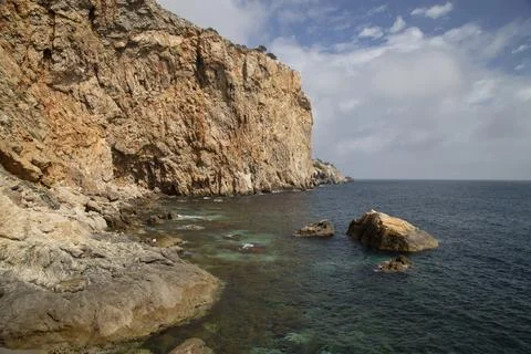 Steep rocky cliffs bordering clear blue mediterranean sea Stock Photos