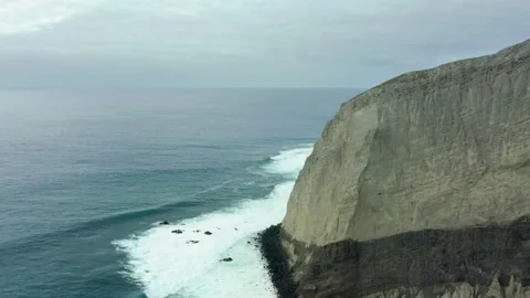 Steep rocky cliffs drop off into coastal waters on overcast day, San Stock Footage 276352222