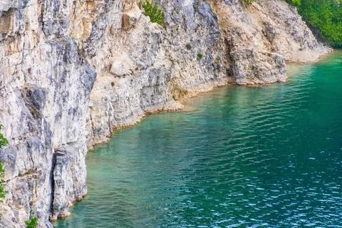 Steep rocky cliffs overlooking clear turquoise water at natural lakeshore Stock Photos